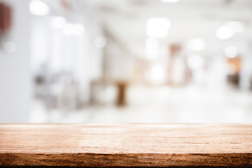 Empty wooden desk space and blurry background of white bokeh light department store for product display montage.