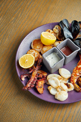 Plate with deep-fried seafood - mussels, octopuses, scallops, squid and shrimp. Antipasto. CLose up view. Wooden background
