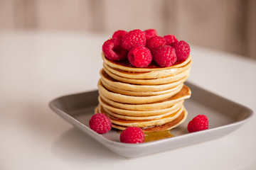 Fresh appetizing raspberries on top of stack of homemade hot pancakes with honey