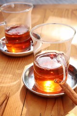 Two glass cups of tea on wooden table on a sunny day. Some cinnamon aside. Closeup, macro, vertical.