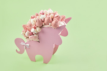 Box in the shape of a unicorn filled with pink sweets, strawberries in chocolate on a green background, copy space