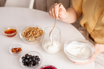 Hand of young casual female putting sourcream into glass during breakfast