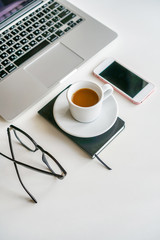 on a table on a white background is a coffee mug, laptop, glasses and a phone