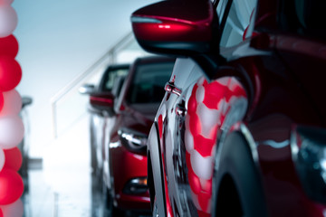 Selective focus red SUV car parked in modern showroom. Car dealership concept. Automotive industry. Auto leasing business. Luxury showroom decor with red and white ballons for promotions and events.