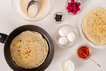Flat layout of frying pan with pancake, fresh eggs, honey, sourcream, berries