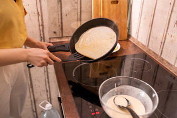 Young housewife with frying pan over electric stove cooking in the kitchen