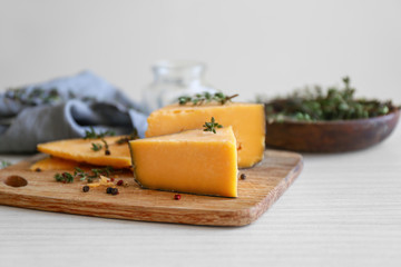 Wooden board with tasty cheese, thyme and spices on white table