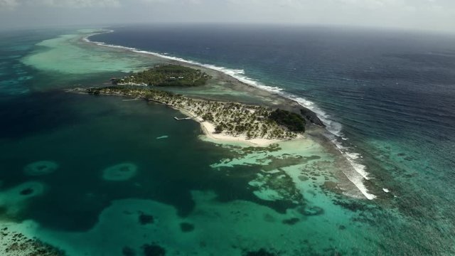 Aerial panning view of waves splashing shore at island, drone flying over beach - Coco Plum Cay, Belize