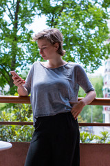 Fototapeta premium Young girl interacting with her phone at her balcony at home on a sunny day.