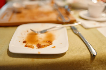 Dish with fork and knife on the table. Empty and dirty plate with bits of food after lunch