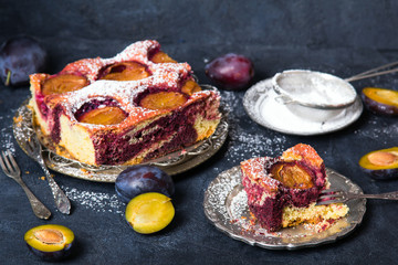 Tasty plum cake with pieces of fruit and powdered sugar on a dark background