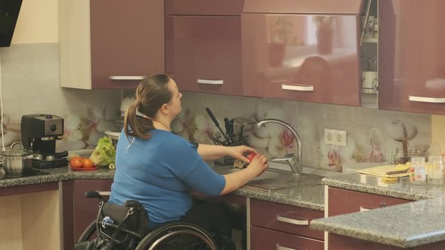 Disabled woman in a wheelchair washes dishes in the kitchen in the wash basin
