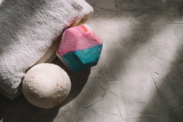 Top view of two bath bombs placed next to a white towel on a gray surface with soft light. Self...