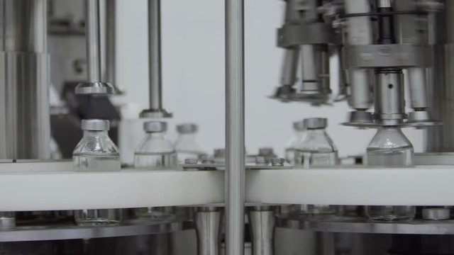 glass bottles filled and sealed with rubber caps on a medical solution conveyor line aluminium cap packaging section selective focus medical industry
