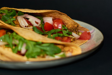 Plate with Mexican cuisine, large tacos with vegetables and meat on black background.
