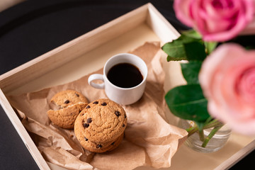 Fresh tasty cookies and cup of black coffee on paper by bunch of pink roses