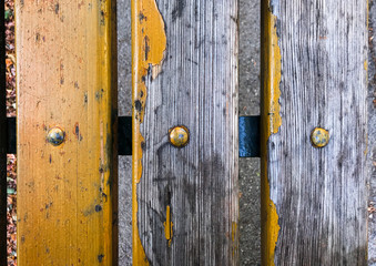 Three old hardwood panel stripes from a bench of a citypark, yellow golden faded paint and rusty metal 