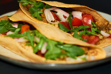 Plate with Mexican cuisine, large tacos with vegetables and meat on black background.
