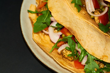 Plate with Mexican cuisine, large tacos with vegetables and meat on black background.