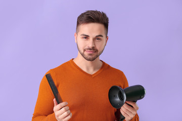 Handsome young man with comb and hair dryer on color background