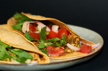 Plate with Mexican cuisine, large tacos with vegetables and meat on black background.