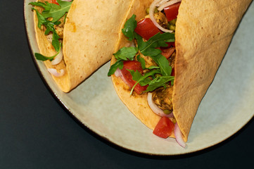 Plate with Mexican cuisine, large tacos with vegetables and meat on black background.