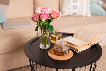 Bunch of pink roses in glass of water, open book, teapot and cup with green tea