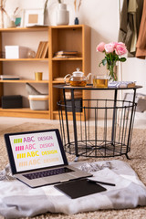 Laptop and pad with stylus on plaid by table with herbal tea and pink roses