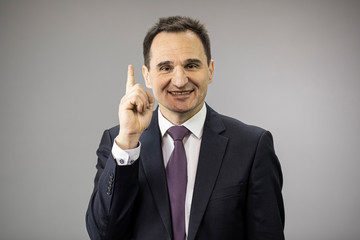 handsome 40s businessman smiling pointing up with his forefinger isolated on gray background copy space. suggestion, best offer, profitable proposition, sale, insurance, investment