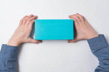 Child hands holding small rectangular blue box. Top view. Copy space