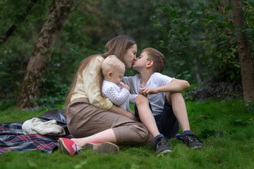 Naklejka na ściany i meble Happy family at picnic. Young mother kisses her older son and holding baby