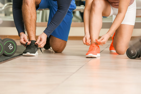 Sporty young couple tying shoelaces in gym in gym - Powered by Adobe