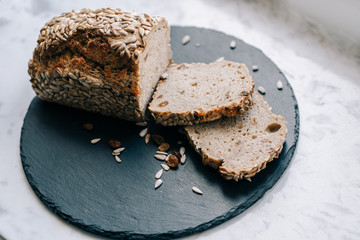fresh home-made dietary rye bread with sunflower seeds and raisins on a black slate board by the window on a light background