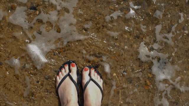 Flip flops on the beach 4K Point of view shot of girls feet with painted nails in flip flops in the north sea UK as waves lap up the shore slow motion.