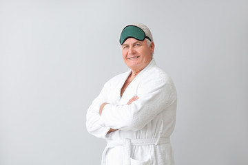 Mature man in bathrobe and with sleep mask on grey background