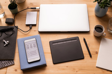 Mobile gadgets, pad with stylus, cup of coffee, notebooks, earphones, etc