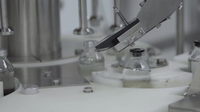 glass bottles filled and sealed with rubber caps on a medical solution conveyor line aluminium cap packaging section close up medical industry