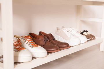 Row of sportive and casual footwear by wall on white lower shelf above the floor