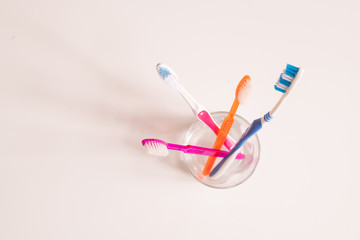 Overview of glass with bunch of new blue, orange and pink toothbrushes