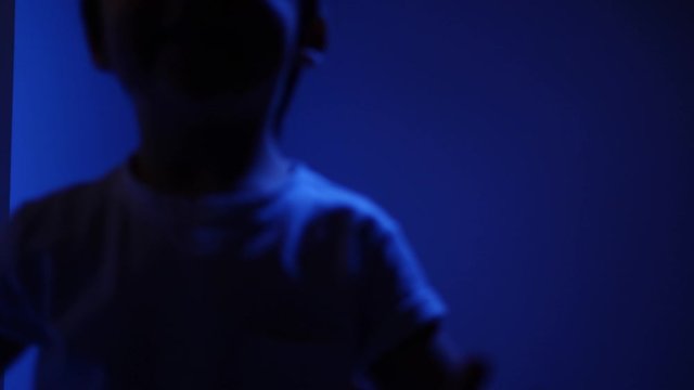 Caucasian child boy dancing at home against the background of a wall with flickering lights blue and red as in a disco