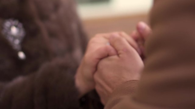A man's hand with a callus in a brown coat holds a woman's hand with a ring, a girl in a fur coat. Winter.
