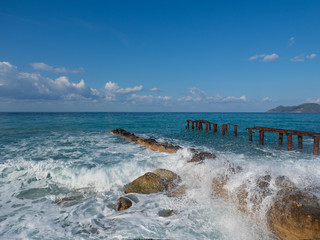 Fototapeta premium Waves breaking on a pier on a sunny day. White foam and splash of sea waves.