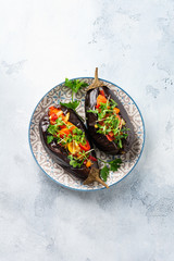 Baked stuffed eggplant with different vegetables, tomato, pepper, onion and parsley on gray stone or concrete table background. Top view.