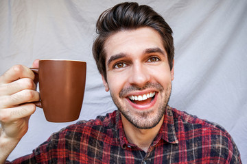 Portrait of a young handsome latin man with a beautiful smile holding a mug of coffee in a shirt 