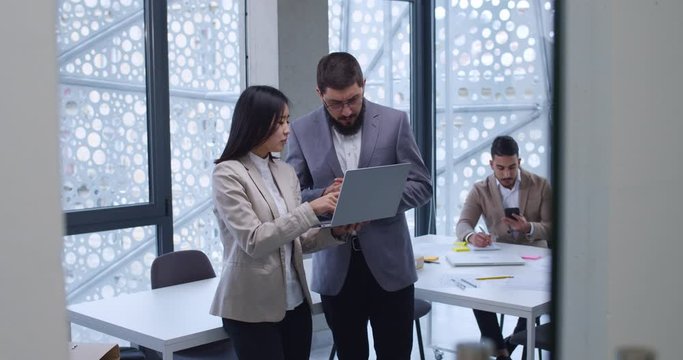 Young Asian woman office worker showing to Caucasian boss her work result. Man approving concept of business strategy. Male and female colleagues of firm gaving discussion.