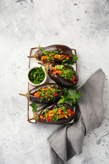 Baked stuffed eggplant with different vegetables, tomato, pepper, onion and parsley on gray stone or concrete table background. Top view.