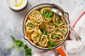 Meat dough rolls with meat or “lazy dumplings” in a cast-iron pan on an old rustic gray background. Top view.