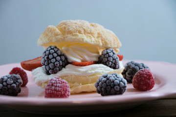 Puff pastry filled with whipped cream, strawberries, blackberries and raspberries on a pink dish. Dessert concept