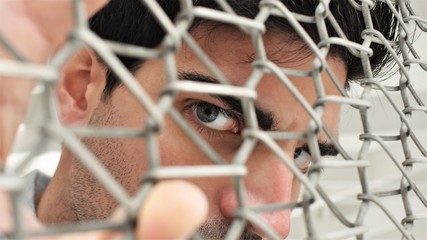 Young man looking away through the mesh of a metal fence. Confinement concept