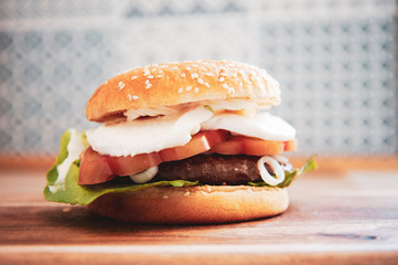 Caprese style hamburger topped with slices of fresh mozzarella cheese, tomato, basil leaves, and lettuce on toasted brioche bun on wooden cutting board. Homemade and healthy sandwich. Italian style.